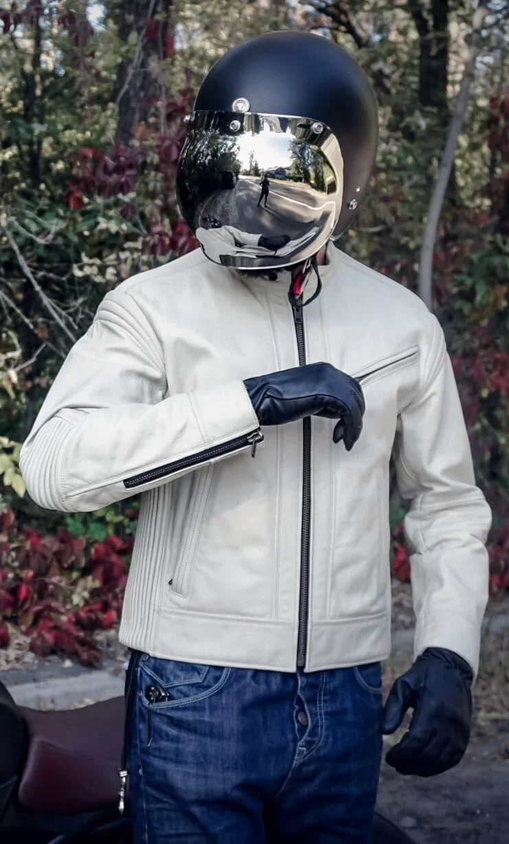 Model wearing a cream cafe racer jacket while riding a motorcycle.