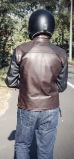 Back view of a man riding a motorcycle wearing a black café racer leather jacket.