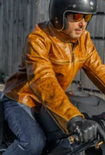 Model riding a motorcycle wearing an orange brown leather racing jacket.